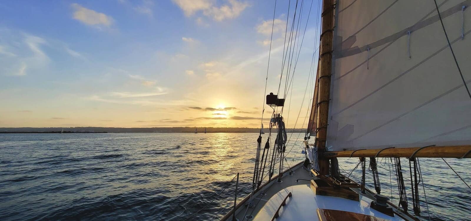 A sailboat heading toward the sun setting over open water